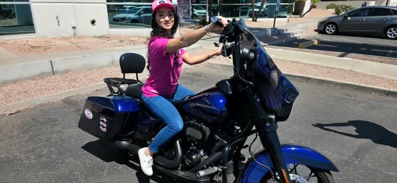 A community member in a pink awareness shirt on a blue motorcycle