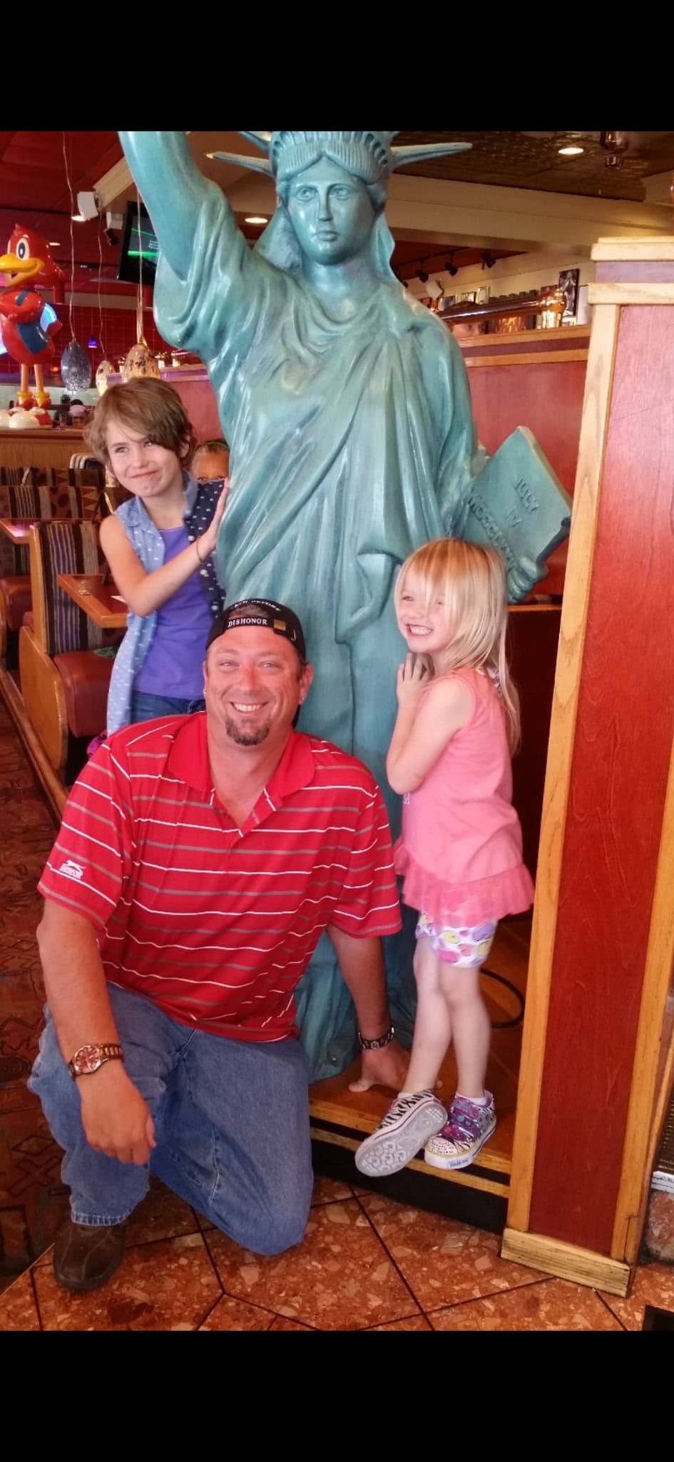 Dube smiling with family beside a Statue of Liberty figure in a restaurant