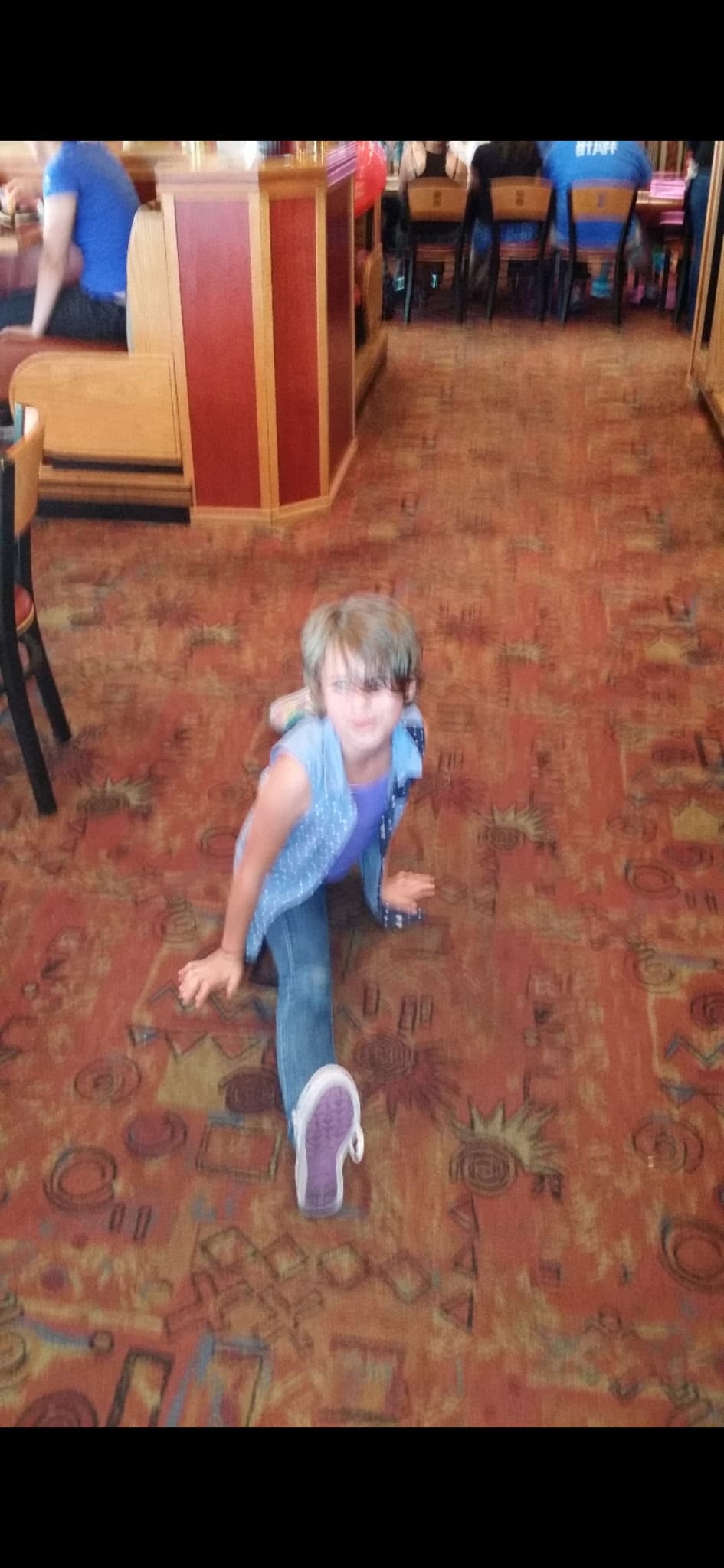 A child in a denim vest and purple top sitting on a restaurant floor with a purple shoe toward the camera