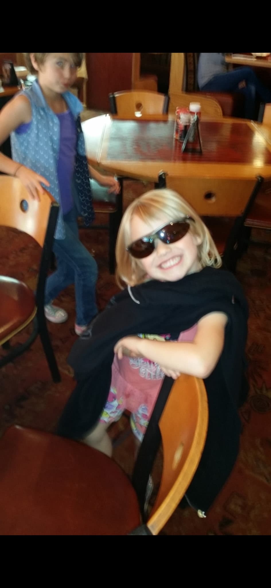 Two children sharing a playful family moment in a restaurant, one smiling in oversized sunglasses